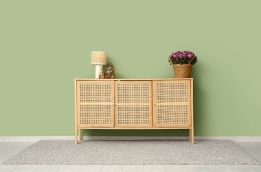 İçinde kasımpatı çiçekleri, lamba ve dekor olan sepet yeşil duvarın yanındaki klozette.