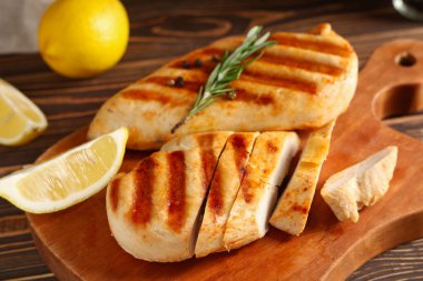 Izgara tavuk göğsü, biberiye, limon dilimi ve ahşap zemin üzerinde biber.