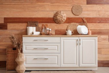 Mutfaktaki ahşap duvarın yanında çatal bıçak ve otlarla dolu beyaz tezgahlar.