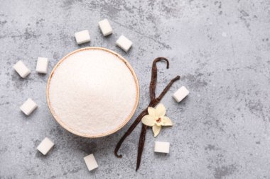 Bir kase vanilya şekeri, kapsüllü ve gri arka planda çiçek.