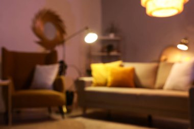 Stil oturma odasının bulanık manzarası rahat gri kanepe, koltuk ve akşamları parlayan lambalar