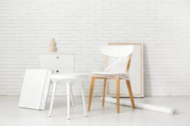 Taşındığı gün beyaz tuğla duvarın yanında streç film olan sarılı sandalye ve masa.