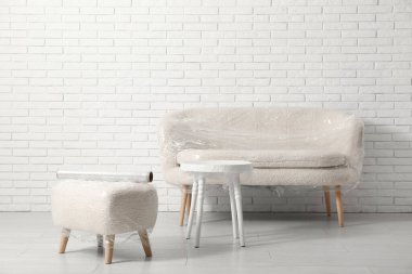 Taşındığı gün beyaz tuğla duvarın yanında streç film olan mobilyalar.