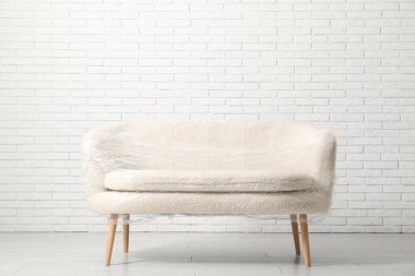 Taşındığı gün beyaz tuğla duvarın yanında streç film olan sarılı kanepe.