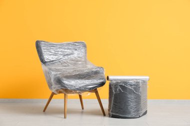 # Sarılı koltuk ve puf # # Taşınma gününde sarı duvarın yanında gerilmiş film #