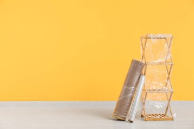 Taşındığı gün sarı duvarın yanında streç film bulunan sarılı raf ve halı.