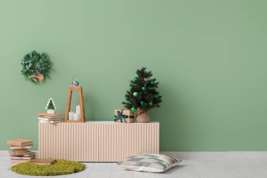 Fenerli Noel ağacı, mumlar, hediye kutusu ve oturma odasındaki yeşil duvarın yanındaki klozette bulunan kitaplar.