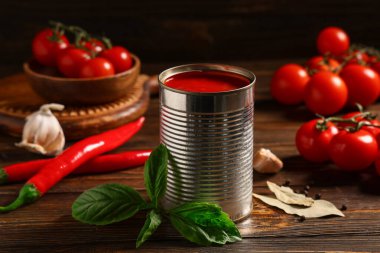 Teneke kutu lezzetli domates ezmesi ve ahşap arka planda farklı malzemeler, yakın plan.