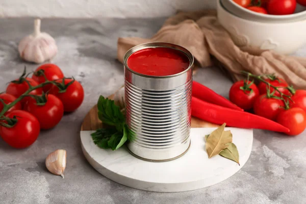 Domates ezmeli teneke kutu ve gri grunge arka planda malzemeler, yakın plan.