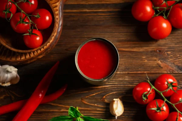 Teneke kutu lezzetli domates ezmesi ve ahşap arka planda farklı malzemeler.