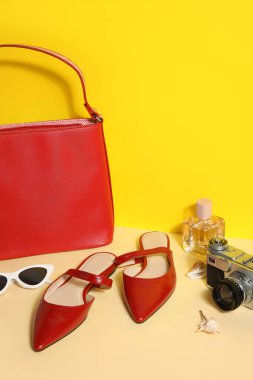 Çantalı kırmızı sandaletler, güneş gözlüğü ve sarı duvarın yanındaki kamera.