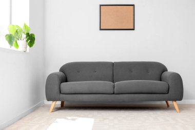 Işıl ışıl oturma odasının içi rahat gri kanepe, pencere pervazında çiçek ve boş çerçeve.