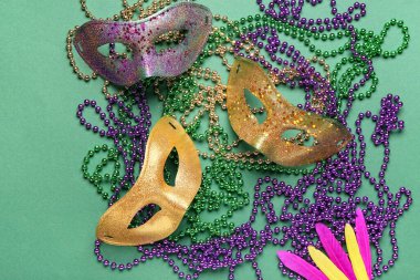 Mardi Gras için yeşil arka planda karnaval maskeleri ve tüyleri olan renkli boncuklar.