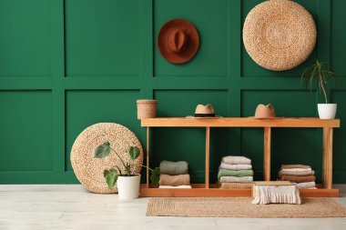 Katlanmış elbiseli ahşap askı, renkli duvarların yanında şapkalar ve bitkiler.