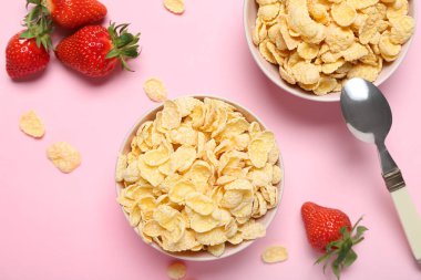 Lezzetli mısır gevrekleri ve pembe arka planda çilekli kaseler, yakın plan.