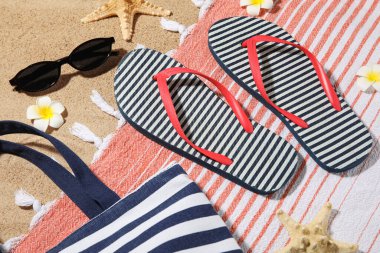 Arka plan olarak kumsalda plaj ayakkabıları ve plaj aksesuarları olan kompozisyon, yakın plan