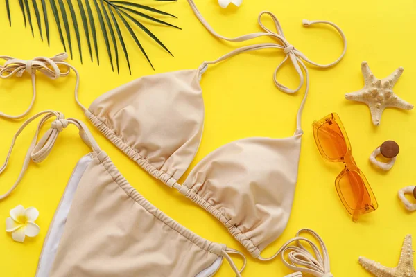 Sarı arka planda şık mayolu ve plaj aksesuarlı kompozisyon, yakın plan.