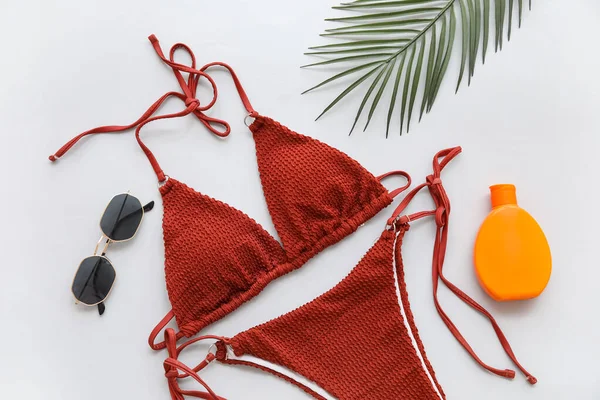 Beyaz arka planda şık bir mayo, güneş gözlüğü ve bir şişe güneş kremi, yakın plan.