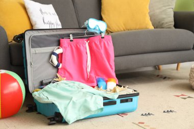 Kanepenin yanında erkek mayosu ve plaj aksesuarları olan bavulu aç.