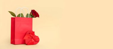 Kırmızı güllü alışveriş torbası ve bej arka planda mesaj için yeri olan hediye. Sevgililer Günü kutlaması