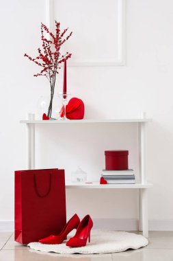 Kırmızı kalp şeklinde hediyesi olan raf ünitesi, alışveriş çantası ve beyaz duvarın yanında ayakkabılar. Sevgililer Günü kutlaması
