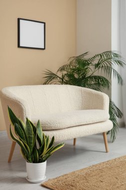 Kanepesi, çiçekleri ve bej duvarında boş resim çerçevesi olan şık bir oturma odası.