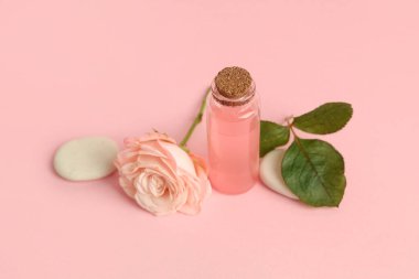 Bir şişe kozmetik yağı, pembe arka planda gül ve spa taşları