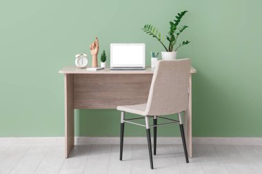 Modern dizüstü bilgisayarı, sandalyesi ve rahat ofisin yeşil duvarının yanındaki bitkisi olan şık bir iş yeri.