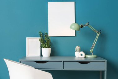 Rahat masalı modern çalışma alanı, şık masa lambası ve mavi duvarın yanındaki ev bitkisi.