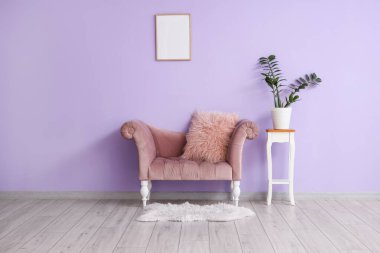 Mor duvarın yanındaki taburede şık bir kanepe ve çiçek var.