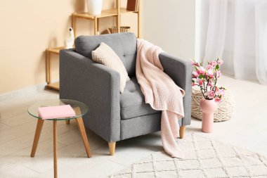 Şık bir oturma odası koltuğu, raf ünitesi ve pembe vazoda güzel çiçekler.