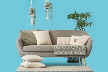 Mavi arka planda battaniyeli, yastıklı ve çiçekli rahat gri kanepe.