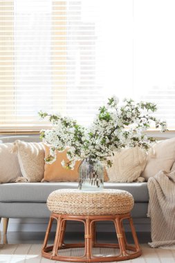 Kanepe, masa ve vazoda çiçek açan dallarla aydınlık oturma odasının içinde.