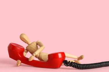 Pembe arka planda telefon alıcısı olan ahşap bir manken.