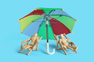 Güverte sandalyelerinde ahşap mankenler ve mavi arka planda plaj şemsiyeleri.