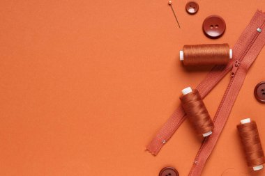 Kahverengi arkaplanda düğmeleri, fermuarı ve top iğnesi olan iplik makaraları