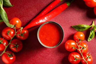 Kırmızı zemin üzerinde fesleğen yaprakları ve kırmızı biberli teneke kutu domates ezmesi.