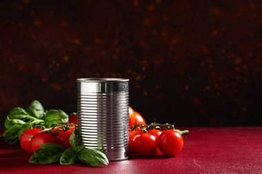 Kırmızı arka planda fesleğen yapraklı ve sebzeli teneke kutu domates ezmesi.
