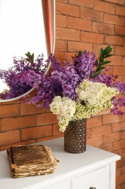 Kahverengi tuğla duvarın yanındaki masada çiçek açan bir vazo ve eski bir kitap.