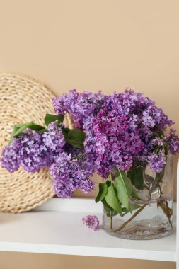 Bej duvarın yanındaki rafta leylak çiçekleri olan vazo.