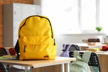 Sınıfta masanın üzerinde elma ve fotokopi kitapları olan sarı sırt çantası.