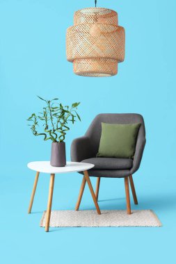 Vazoda bambu saplı masa, koltuk, halı ve lamba mavi arka planda.