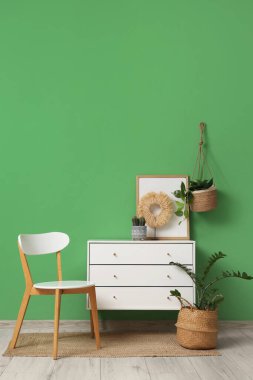 Yeşil duvarın yanında sandıklı ve sandalyeli modern tarz bir oda.