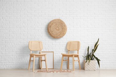 Sandalyeler, bitki örtüsü ve fotoğraf çerçevesi modern odanın içindeki beyaz tuğla duvarın yanında.