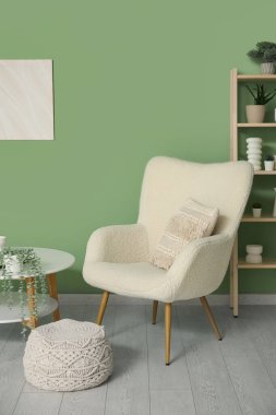 Interior of living room with table, pouf and soft armchair near green wall, closeup