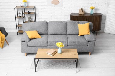 Rahat kanepe, şifonyer, sehpa ve narsis çiçekleri oturma odasındaki beyaz tuğla duvara karşı.