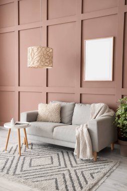 Oturma odasının iç tarafındaki kahverengi duvarın yanında rahat bir kanepe, masa ve çiçek var.