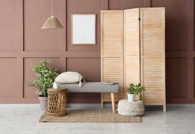 Oturma odasının iç tarafındaki kahverengi duvarın yanındaki benç, katlanan ekran ve bitkiler.