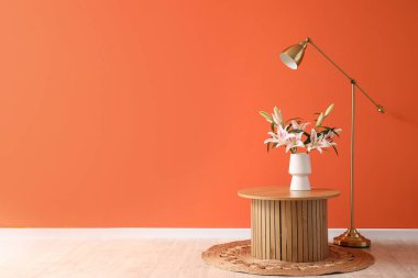 Bir buket çiçekli ahşap sehpa ve turuncu duvarın yanında standart lamba.