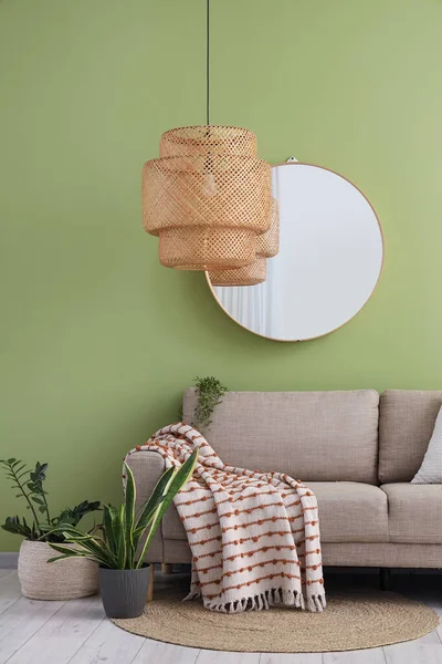 Yeşil duvarın yanında rahat gri kanepesi, çiçekleri ve aynası olan şık bir oturma odası.